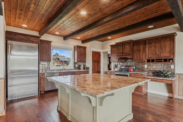 kitchen with a breakfast bar, light stone counters, a kitchen island, stainless steel appliances, and beam ceiling