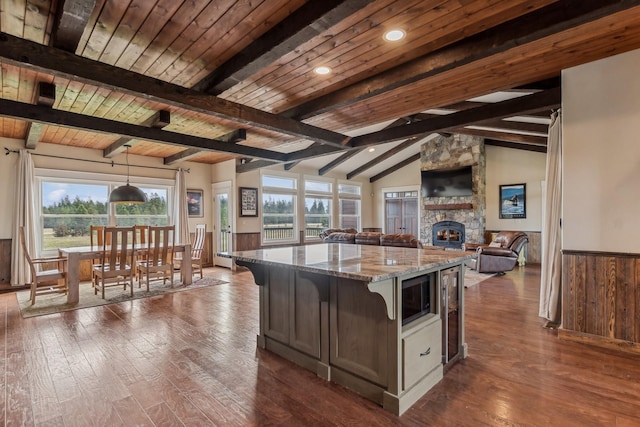 kitchen with a stone fireplace, a center island, lofted ceiling with beams, pendant lighting, and light stone countertops