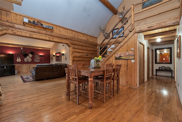 dining area with wood-type flooring, vaulted ceiling with beams, wooden walls, and rustic walls