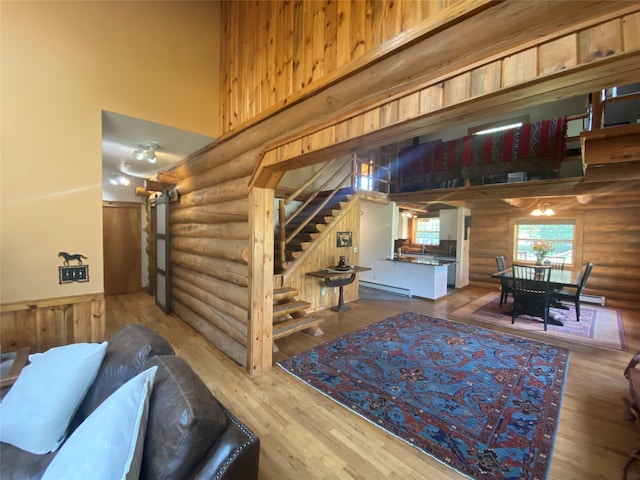 living room with a high ceiling, log walls, hardwood / wood-style floors, and a baseboard heating unit