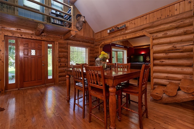 dining area featuring log walls, hardwood / wood-style floors, and high vaulted ceiling