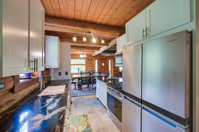 kitchen featuring beamed ceiling, stainless steel appliances, light tile patterned floors, and white cabinetry