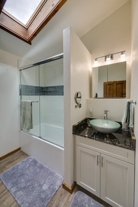 bathroom with enclosed tub / shower combo, hardwood / wood-style floors, vanity, and vaulted ceiling