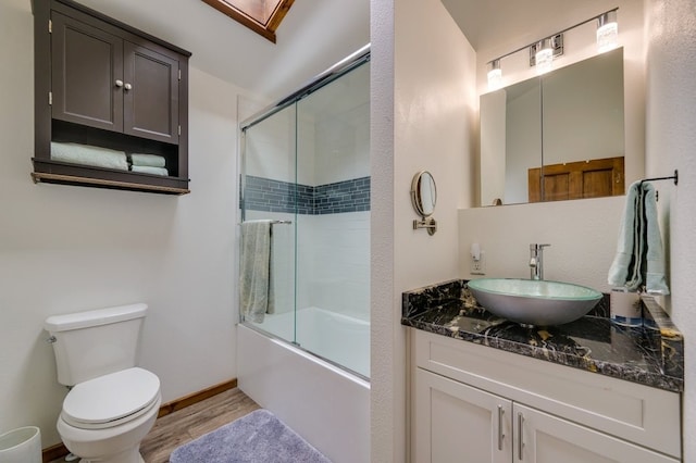 full bathroom featuring hardwood / wood-style floors, combined bath / shower with glass door, vanity, and toilet