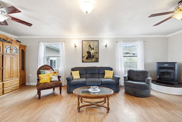 living room featuring light wood-type flooring, ornamental molding, ceiling fan, and a wood stove