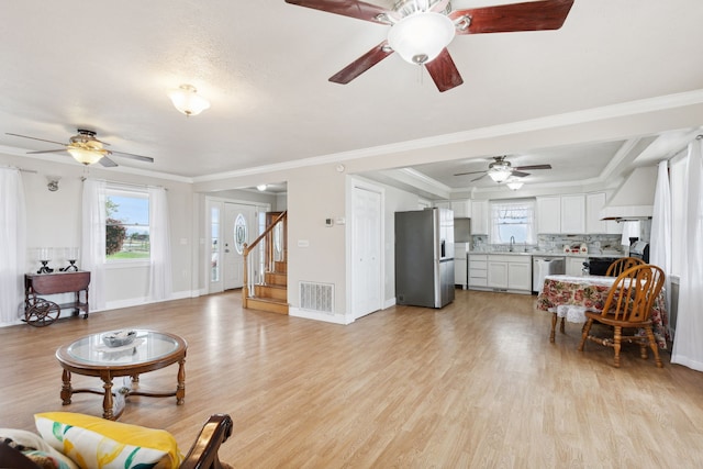 living room with light wood-type flooring, crown molding, sink, and ceiling fan