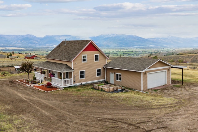 view of front facade featuring a mountain view, a garage, an outbuilding, a rural view, and covered porch