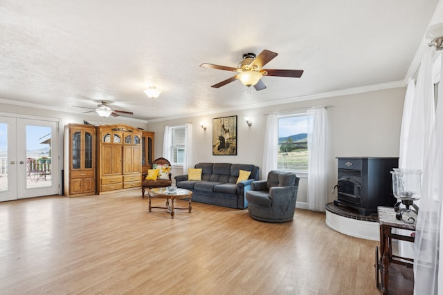 living room with ceiling fan, ornamental molding, a wood stove, french doors, and light hardwood / wood-style floors