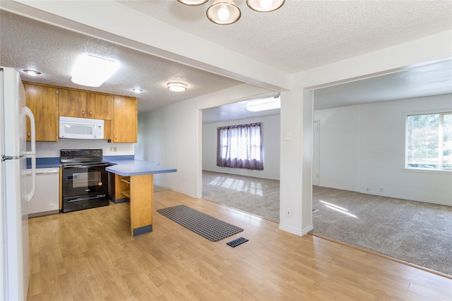 kitchen with a textured ceiling, white appliances, a breakfast bar area, and light hardwood / wood-style flooring