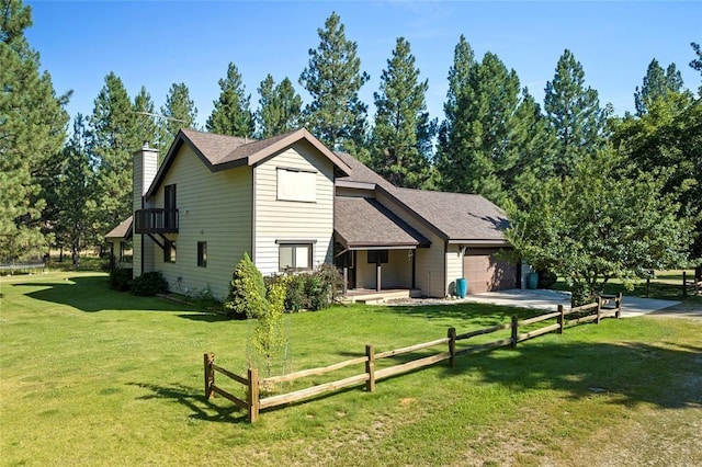 back of property with an attached garage, a balcony, a yard, driveway, and a chimney