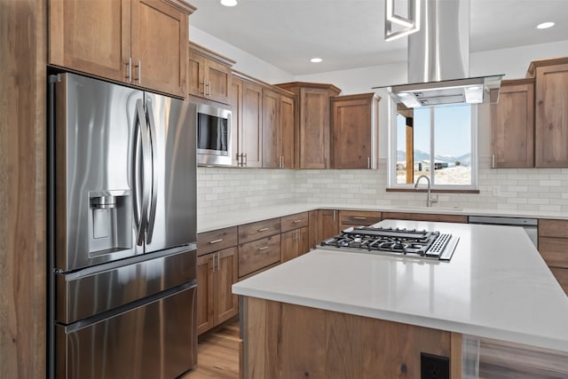 kitchen featuring sink, tasteful backsplash, island range hood, a center island, and appliances with stainless steel finishes