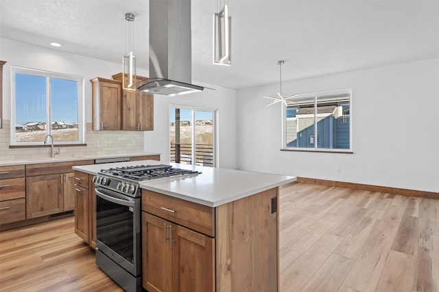 kitchen featuring sink, a center island, gas stove, island exhaust hood, and decorative light fixtures