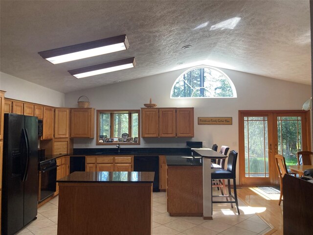 kitchen featuring black appliances, lofted ceiling, a center island, and plenty of natural light