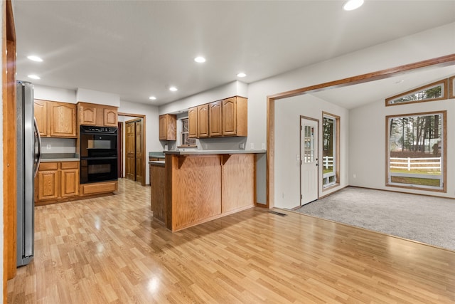 kitchen featuring a kitchen breakfast bar, black double oven, vaulted ceiling, kitchen peninsula, and stainless steel refrigerator