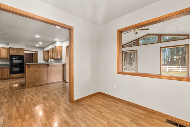 kitchen with lofted ceiling, ceiling fan, light wood-type flooring, double oven, and kitchen peninsula