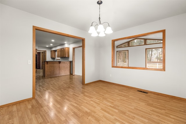 empty room with a notable chandelier and light hardwood / wood-style floors