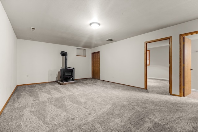 unfurnished living room with light colored carpet and a wood stove