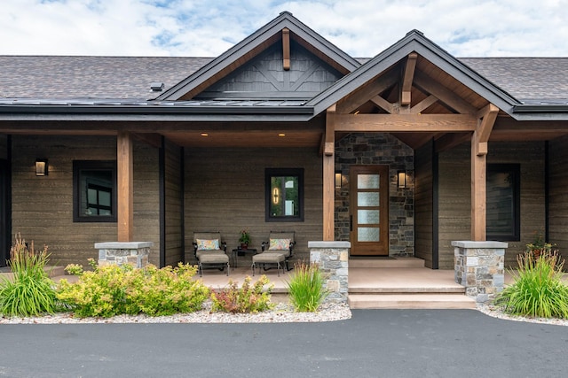 property entrance featuring roof with shingles, a porch, and stone siding