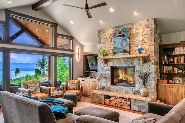 living room with beamed ceiling, a stone fireplace, a ceiling fan, and wood finished floors