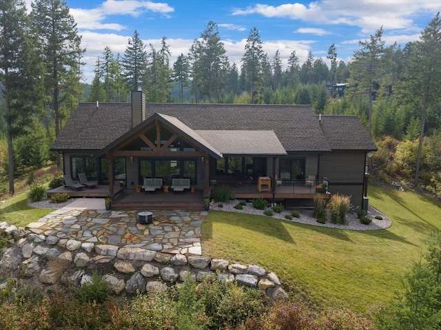 rear view of house with a lawn, a deck, a chimney, and roof with shingles