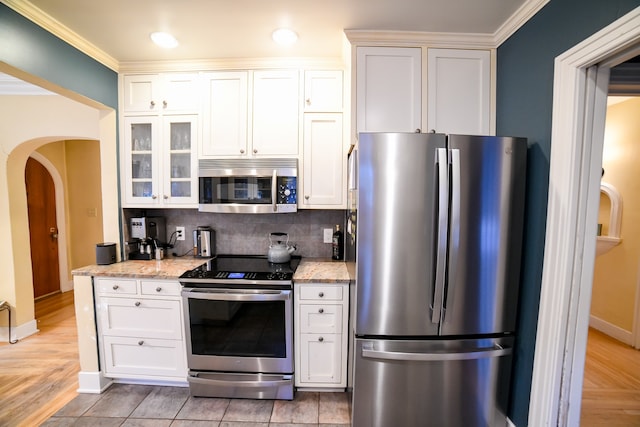 kitchen featuring appliances with stainless steel finishes, light stone counters, tasteful backsplash, white cabinets, and crown molding