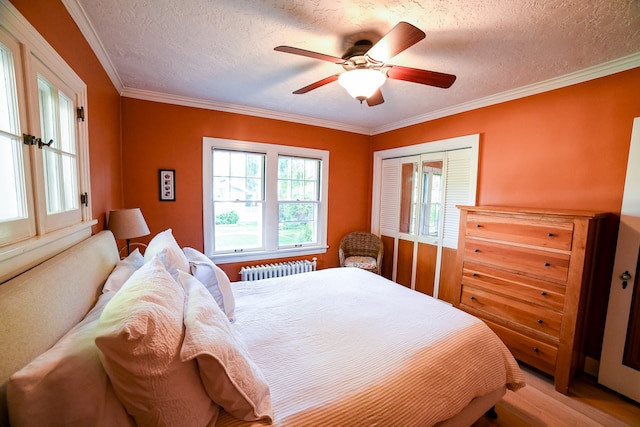 bedroom with light hardwood / wood-style floors, radiator heating unit, a closet, crown molding, and ceiling fan