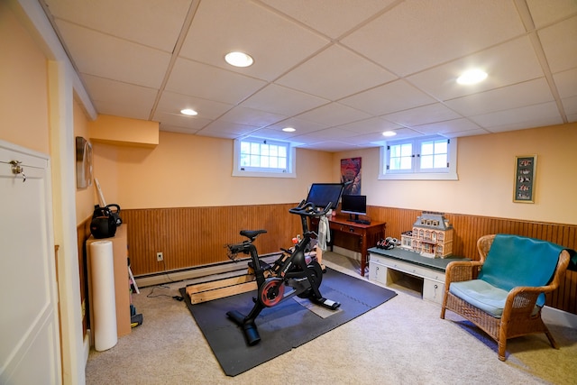 exercise room with a drop ceiling, a baseboard heating unit, wood walls, and light carpet