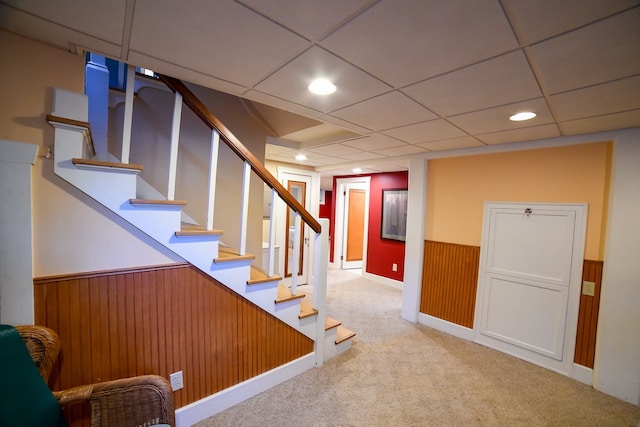 basement featuring a drop ceiling, wood walls, and light carpet