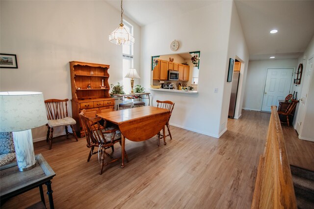 dining room featuring a notable chandelier, a towering ceiling, and light hardwood / wood-style floors