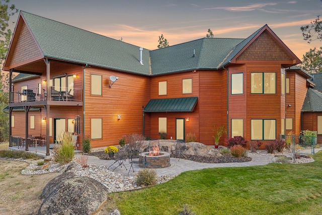 back house at dusk featuring a yard, a balcony, a patio, and an outdoor fire pit