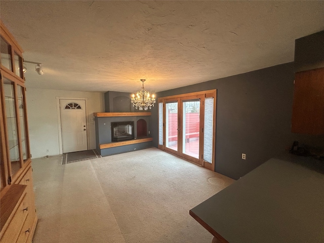 unfurnished living room with light carpet, a textured ceiling, and a chandelier