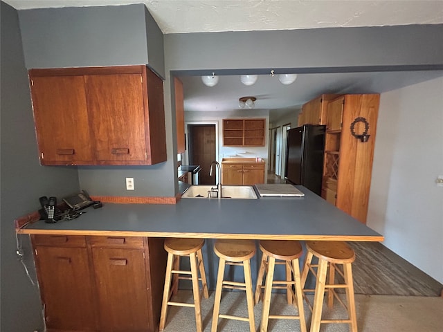 kitchen featuring black refrigerator, a kitchen bar, kitchen peninsula, and sink