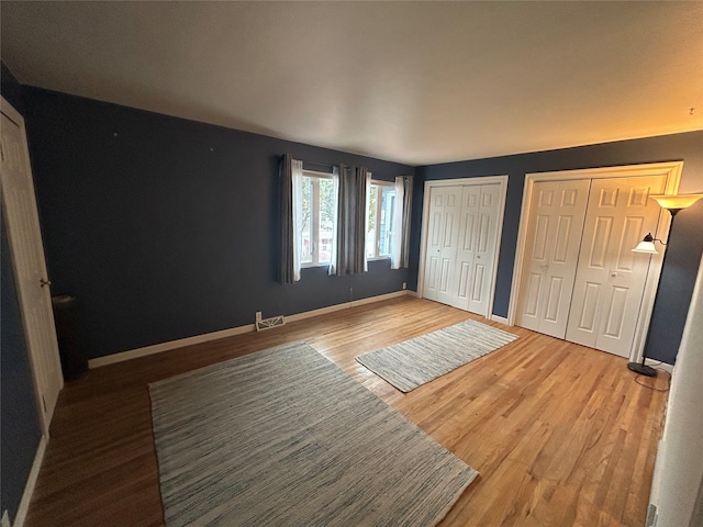 unfurnished bedroom featuring hardwood / wood-style flooring and two closets