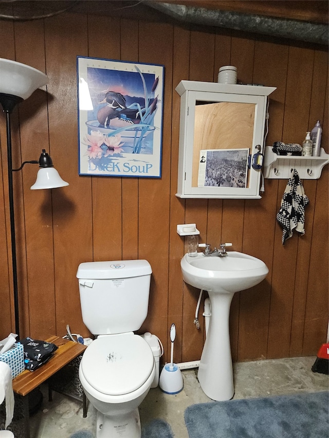 bathroom with wood walls, toilet, and concrete floors