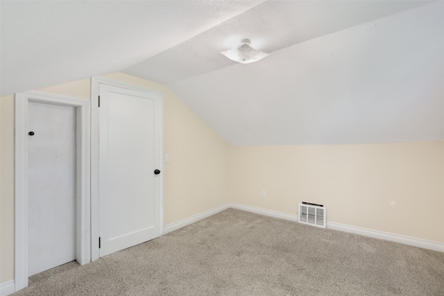 additional living space featuring a textured ceiling, vaulted ceiling, and light carpet