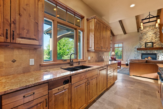 kitchen featuring tasteful backsplash, a stone fireplace, light stone countertops, vaulted ceiling with beams, and sink