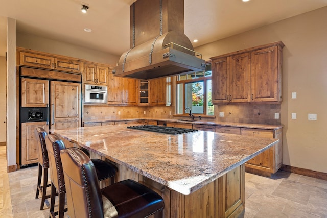 kitchen featuring light stone counters, tasteful backsplash, island range hood, a kitchen island, and stainless steel appliances