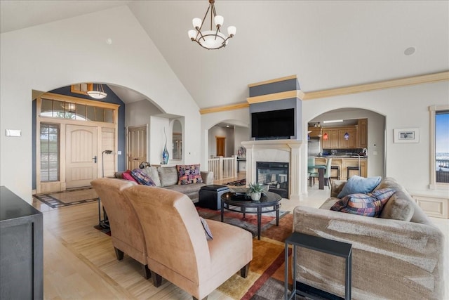 living area featuring a premium fireplace, arched walkways, high vaulted ceiling, and a chandelier