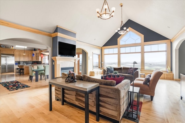 living room with a fireplace, light wood-type flooring, high vaulted ceiling, and a chandelier