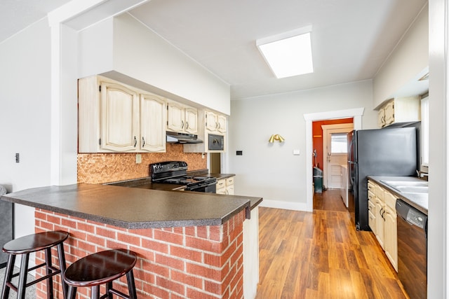 kitchen featuring a breakfast bar, light wood-type flooring, kitchen peninsula, decorative backsplash, and black appliances