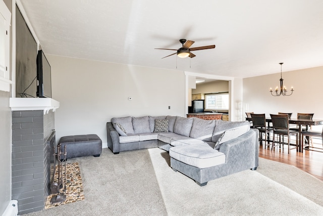 carpeted living room with ceiling fan with notable chandelier and a fireplace