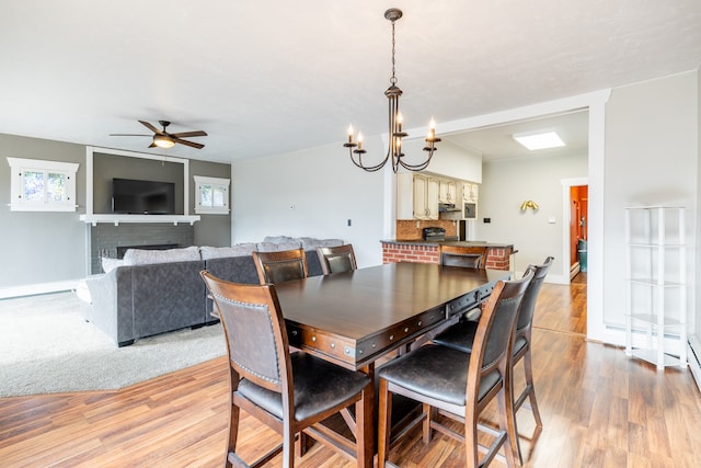 dining space featuring a brick fireplace, ceiling fan with notable chandelier, and light hardwood / wood-style flooring