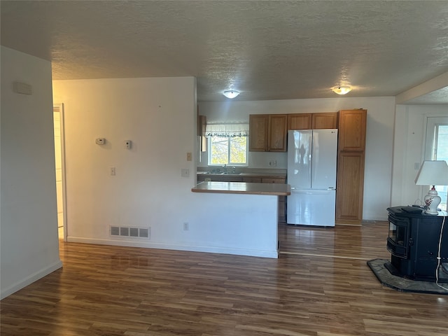 kitchen with sink, a textured ceiling, a wood stove, dark wood-type flooring, and white fridge