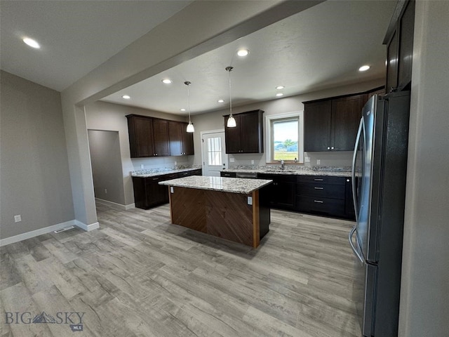 kitchen with sink, hanging light fixtures, a kitchen island, stainless steel refrigerator, and light hardwood / wood-style flooring