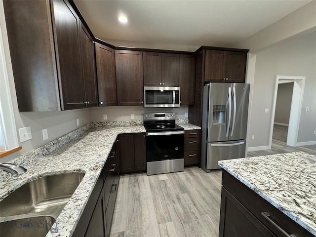 kitchen with dark brown cabinetry, light stone counters, sink, light hardwood / wood-style flooring, and appliances with stainless steel finishes