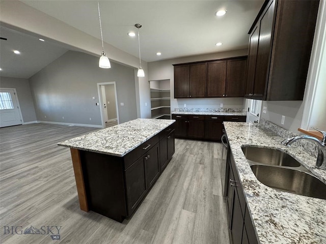 kitchen featuring sink, vaulted ceiling, a kitchen island, light hardwood / wood-style flooring, and light stone countertops