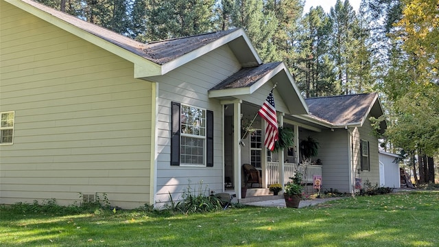 view of side of property with roof with shingles, a porch, and a lawn