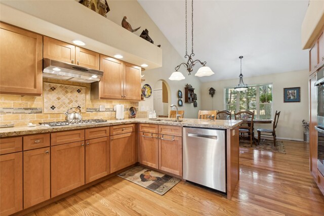 kitchen with kitchen peninsula, stainless steel appliances, backsplash, decorative light fixtures, and sink