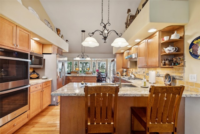 kitchen featuring a peninsula, a sink, appliances with stainless steel finishes, light stone countertops, and open shelves