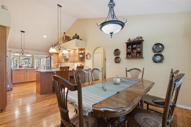 dining space featuring light wood-style floors, arched walkways, and high vaulted ceiling